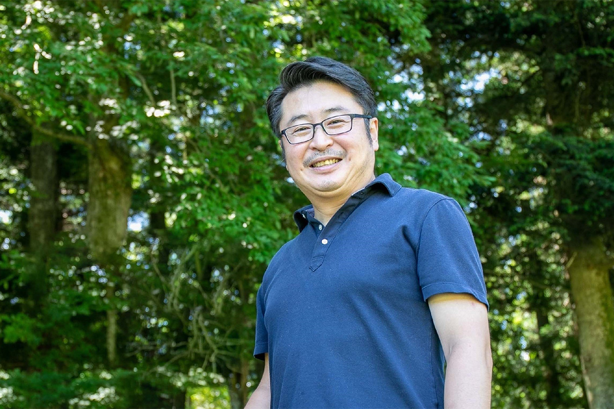 緑豊かな自然の中で笑顔を見せる、マインドテック株式会社の開発顧問・ITアーキテクト 本間紀史の画像